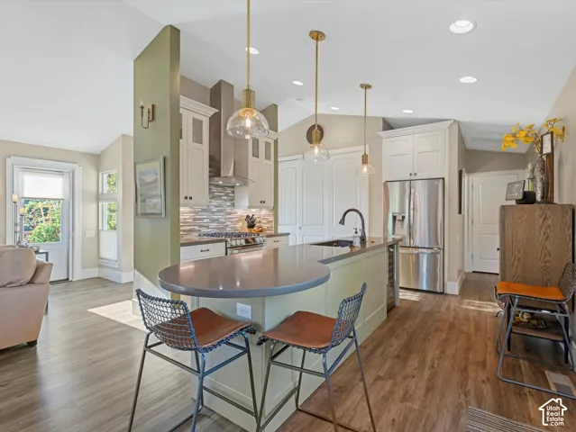 Kitchen featuring lofted ceiling, stainless steel appliances, decorative backsplash, white cabinetry, and wall chimney exhaust hood