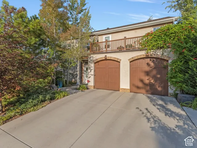 View of front facade featuring stucco siding, a balcony, concrete driveway, and a two-car garage