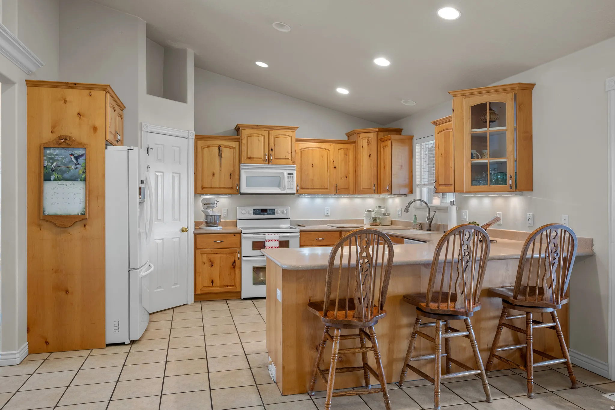 Kitchen featuring wood cabinetry, white appliances, and bar seating