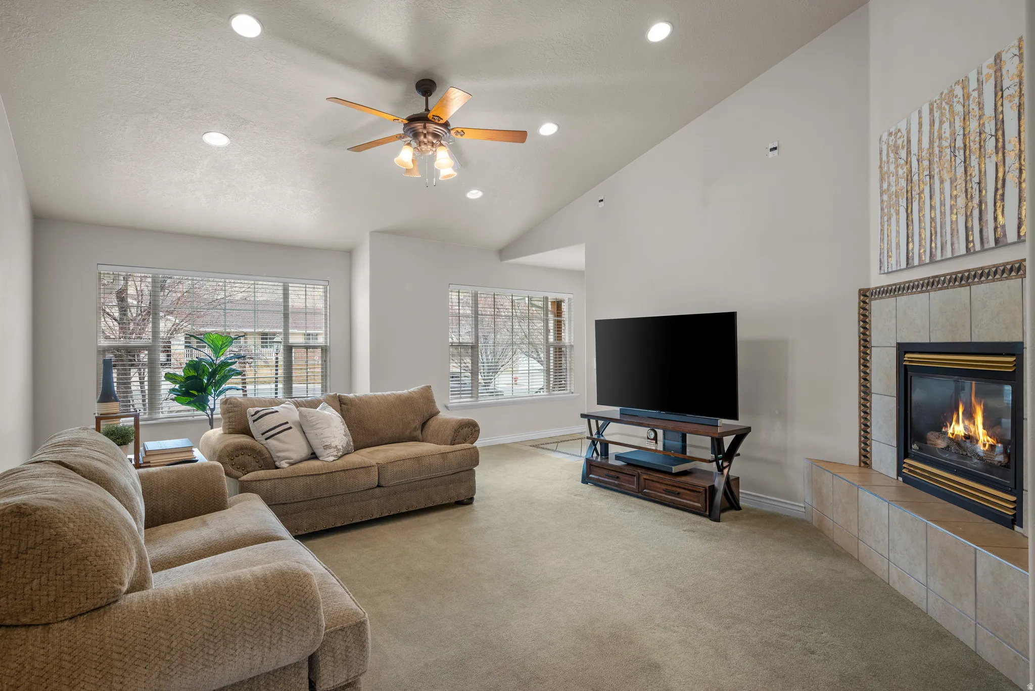 Living room featuring a gas fireplace with a tiled surround, vaulted ceilings, recessed lighting, and a ceiling fan