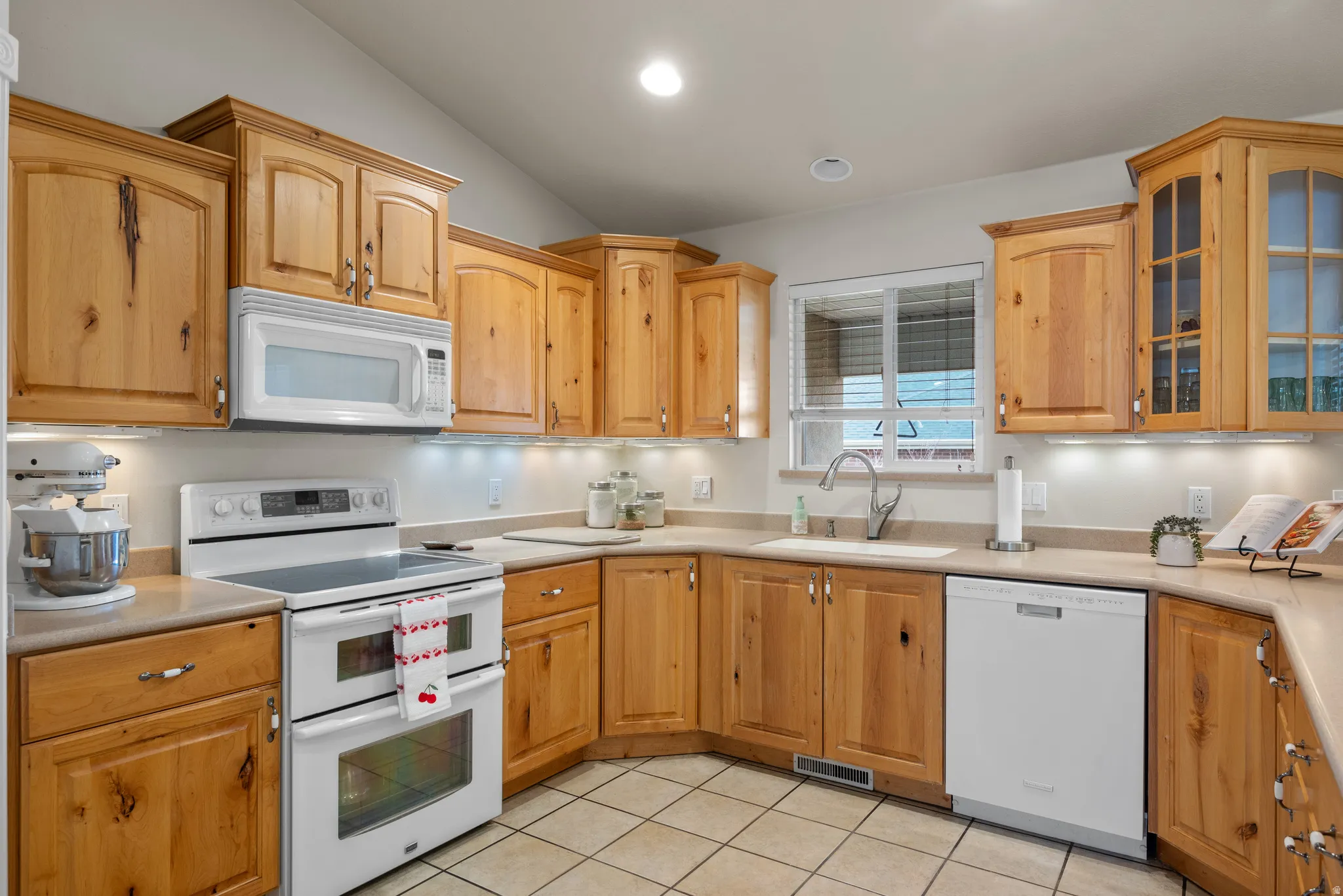 Kitchen featuring wood cabinetry, corian countertops, white appliances, and tile floor