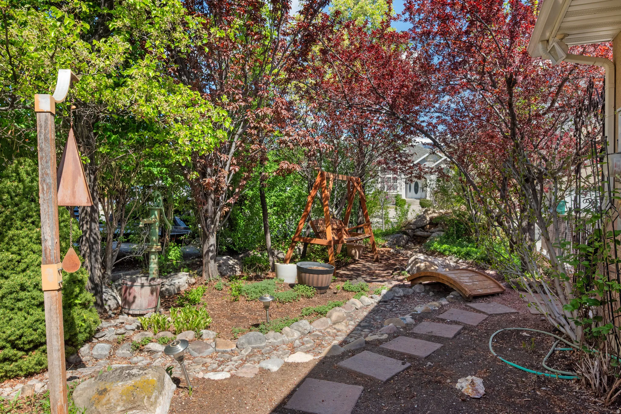 Landscaped backyard featuring mature trees, a wooden swing, and a decorative garden bridge (This is known as the "Secret Garden".)