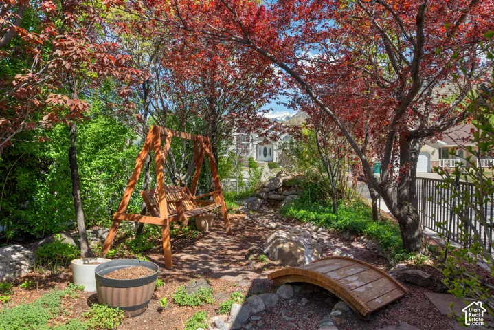 Landscaped garden area featuring a wooden swing, a decorative footbridge, and vibrant red-leafed trees (Secret Garden)