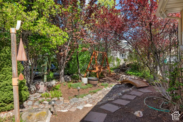Landscaped backyard featuring mature trees, a wooden swing, and a decorative garden bridge (This is known as the "Secret Garden".)