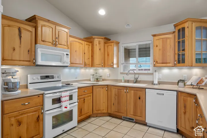 Kitchen featuring wood cabinetry, corian countertops, white appliances, and tile floor