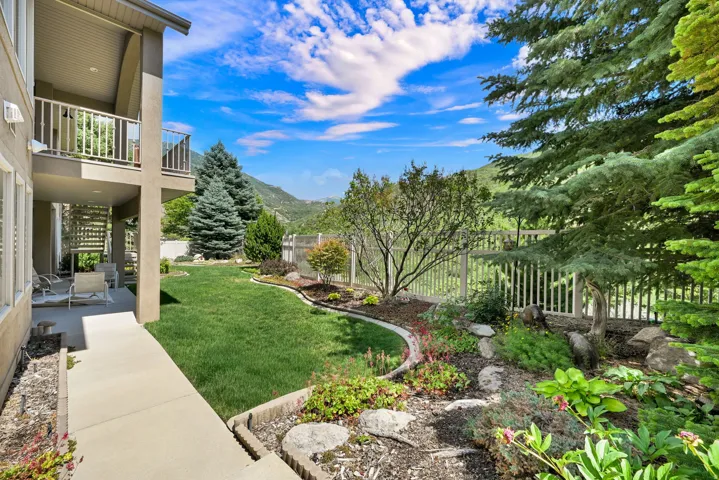 Landscaped backyard with mature trees, a manicured lawn, and mountain scenery.