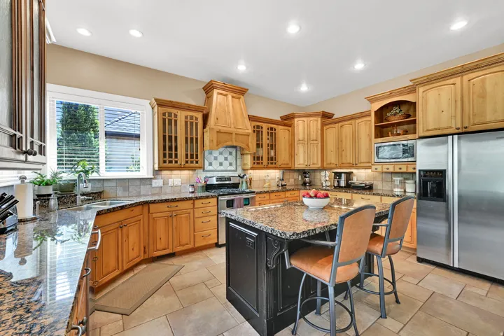 Natural wood cabinetry, granite countertops, a central island, stainless steel appliances, and tile flooring.