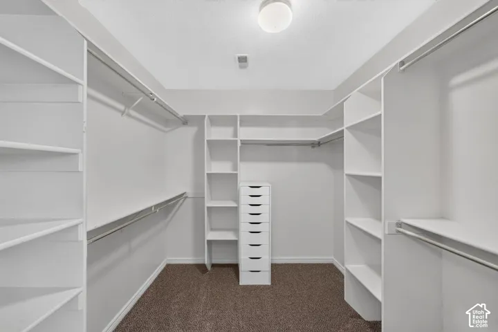 Walk-in closet with extensive white shelving, multiple hanging rods, and a central drawer unit