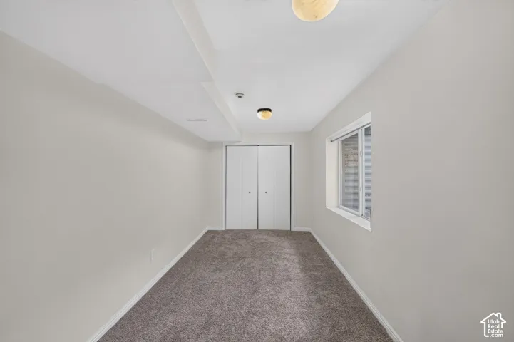 Carpeted room featuring a white bi-fold closet, a window with horizontal blinds, and two ceiling-mounted light fixtures