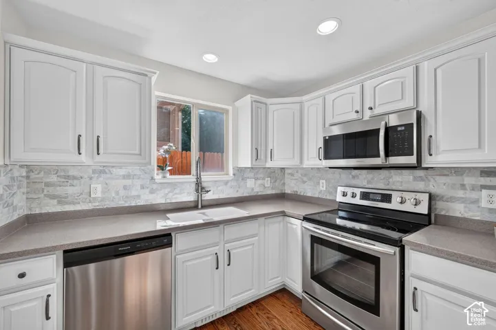 Kitchen featuring white cabinetry, stainless steel appliances, a tile backsplash, and a window above the sink