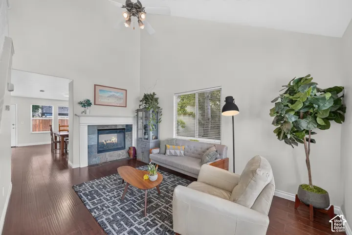 Vaulted ceiling living room featuring a fireplace with stone surround, wood mantel, dark wood-finish flooring, and a ceiling fan