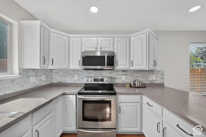 U-shaped kitchen featuring white cabinetry with dark hardware, a stone-finish backsplash, and light-toned countertops