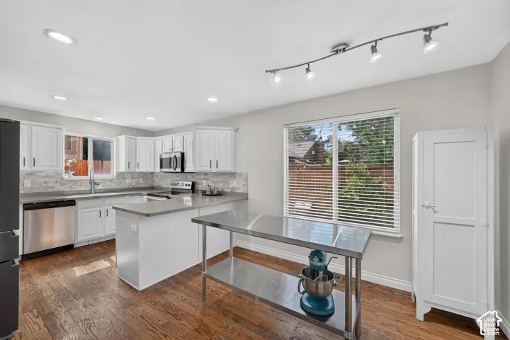 Spacious kitchen featuring wood-finish flooring, white cabinetry, stainless steel appliances, and a light-toned countertop