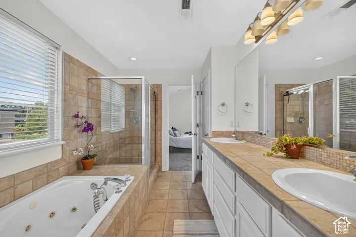 Bathroom featuring a jetted soaking tub, a glass-enclosed shower, and a dual vanity with tile countertops