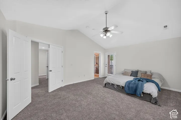Spacious bedroom featuring vaulted ceilings, plush carpet flooring, a ceiling fan with integrated lighting, a white panel door leading to an outdoor area, and double white panel doors