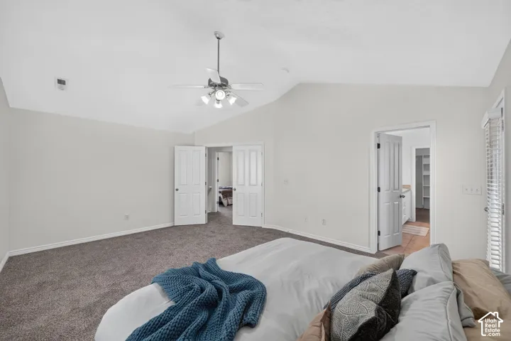 Spacious room featuring vaulted ceilings, a ceiling fan with integrated lighting, plush gray carpeting, and multiple white paneled doors
