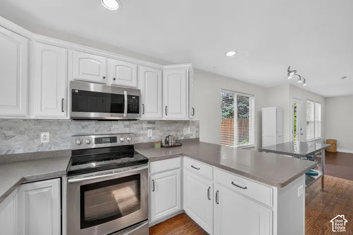 Contemporary kitchen featuring white cabinetry, stainless steel appliances, a tile backsplash, and solid surface countertops