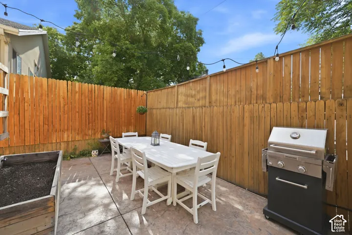 Private patio space with stamped concrete flooring, tall wood fencing, and string lighting