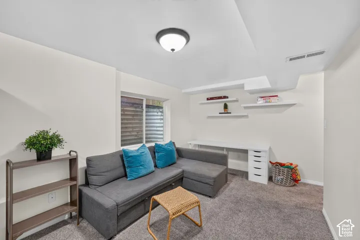 Carpeted room featuring a white-framed window, built-in desk with drawer storage, and white floating wall shelves