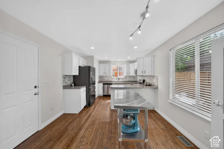 Spacious kitchen featuring wood-finish flooring, white cabinetry, dark countertops, a tile backsplash, and stainless steel appliances