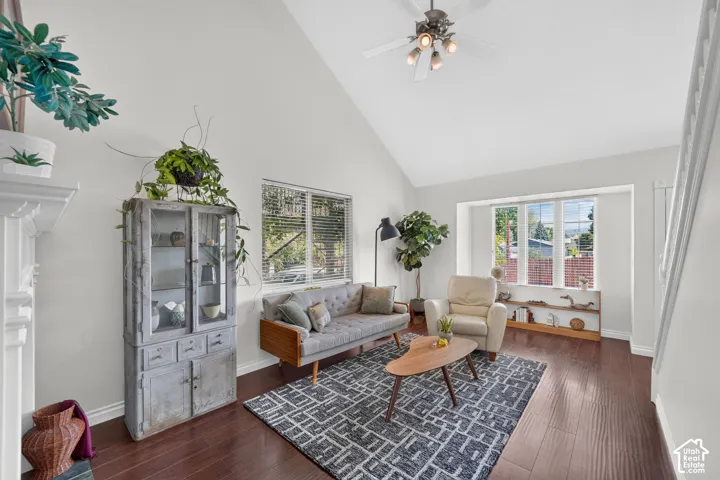 Vaulted ceilings in this living space featuring dark wood-finish flooring, a prominent bay window, and a white ceiling fan with integrated lighting