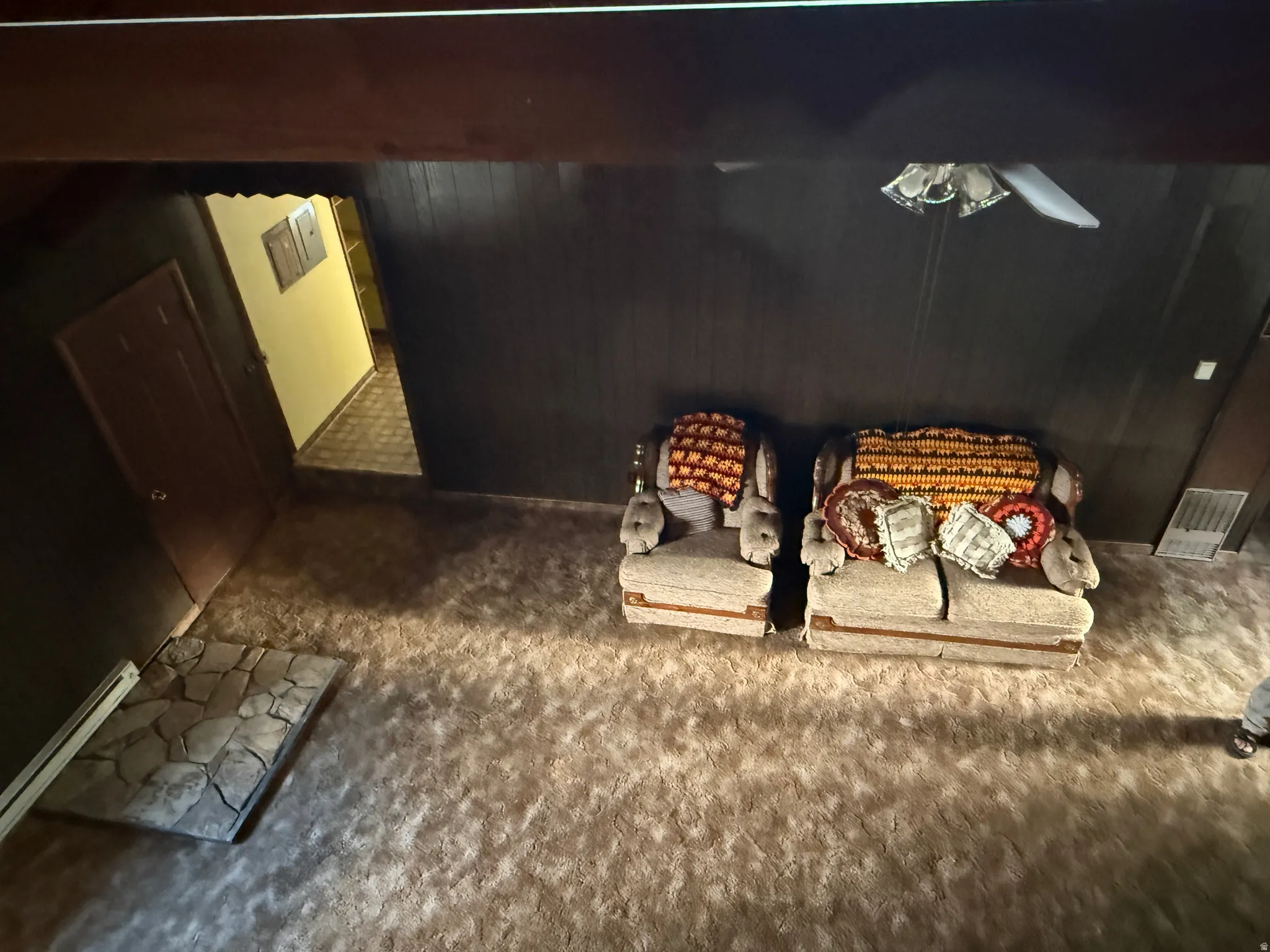 Spacious room featuring textured carpet flooring, dark wood-paneled walls, and a recessed stone-finish floor mat