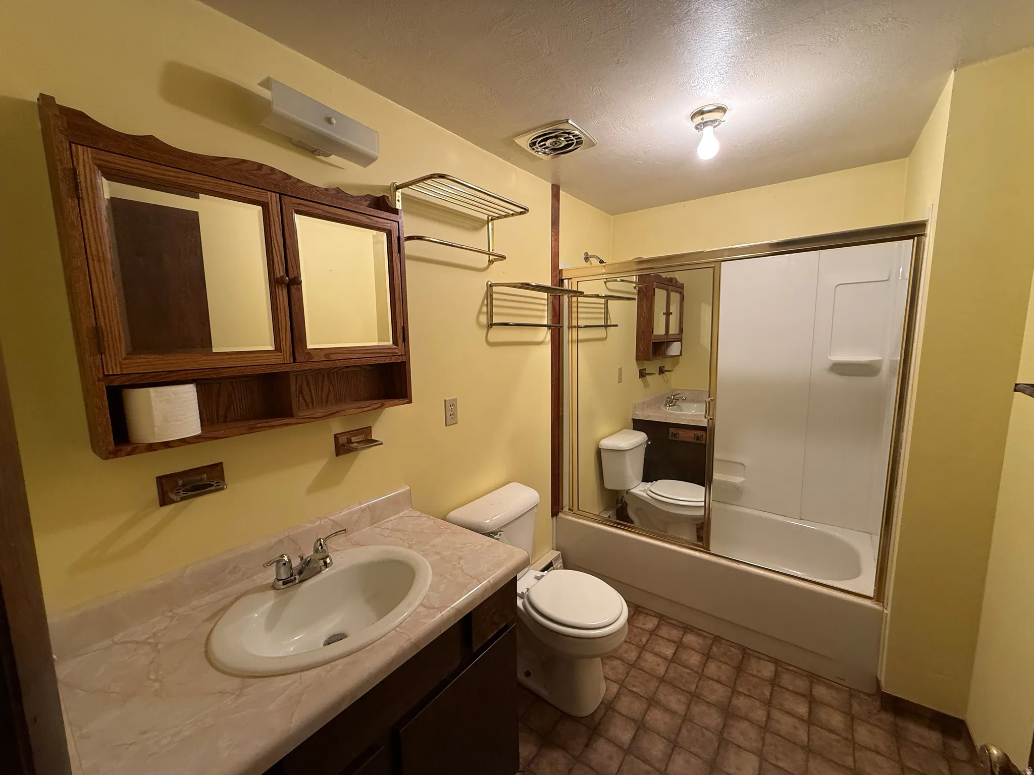 Bathroom featuring a vanity with an integrated sink, a medicine cabinet, an enclosed bathtub with shower, and patterned flooring