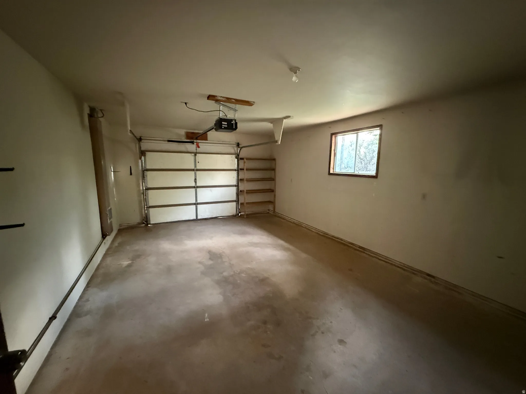 Spacious garage featuring a concrete floor, overhead garage door with opener, built-in shelving, and a window
