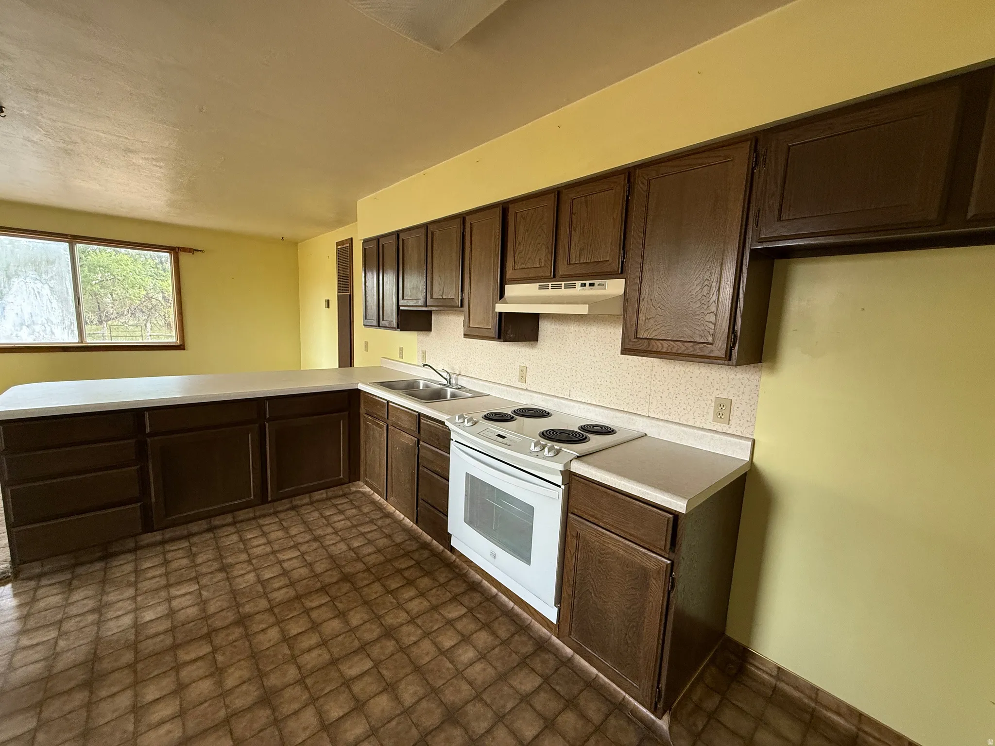 Kitchen featuring extensive dark wood-finish cabinetry, a white electric range, a dual-basin stainless steel sink, and light-toned countertops