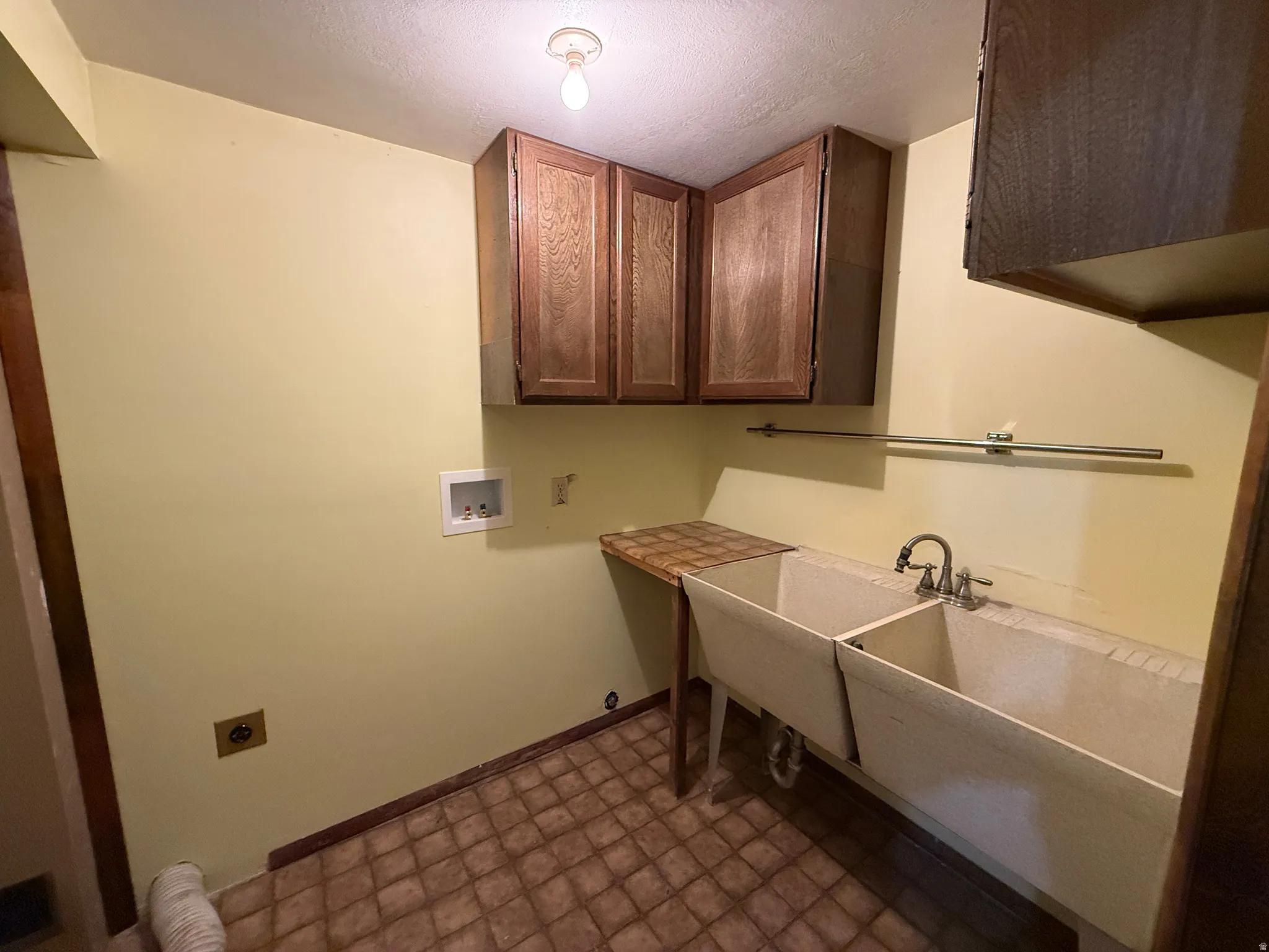 Utility room featuring a double basin sink, overhead cabinetry, and laundry hookups