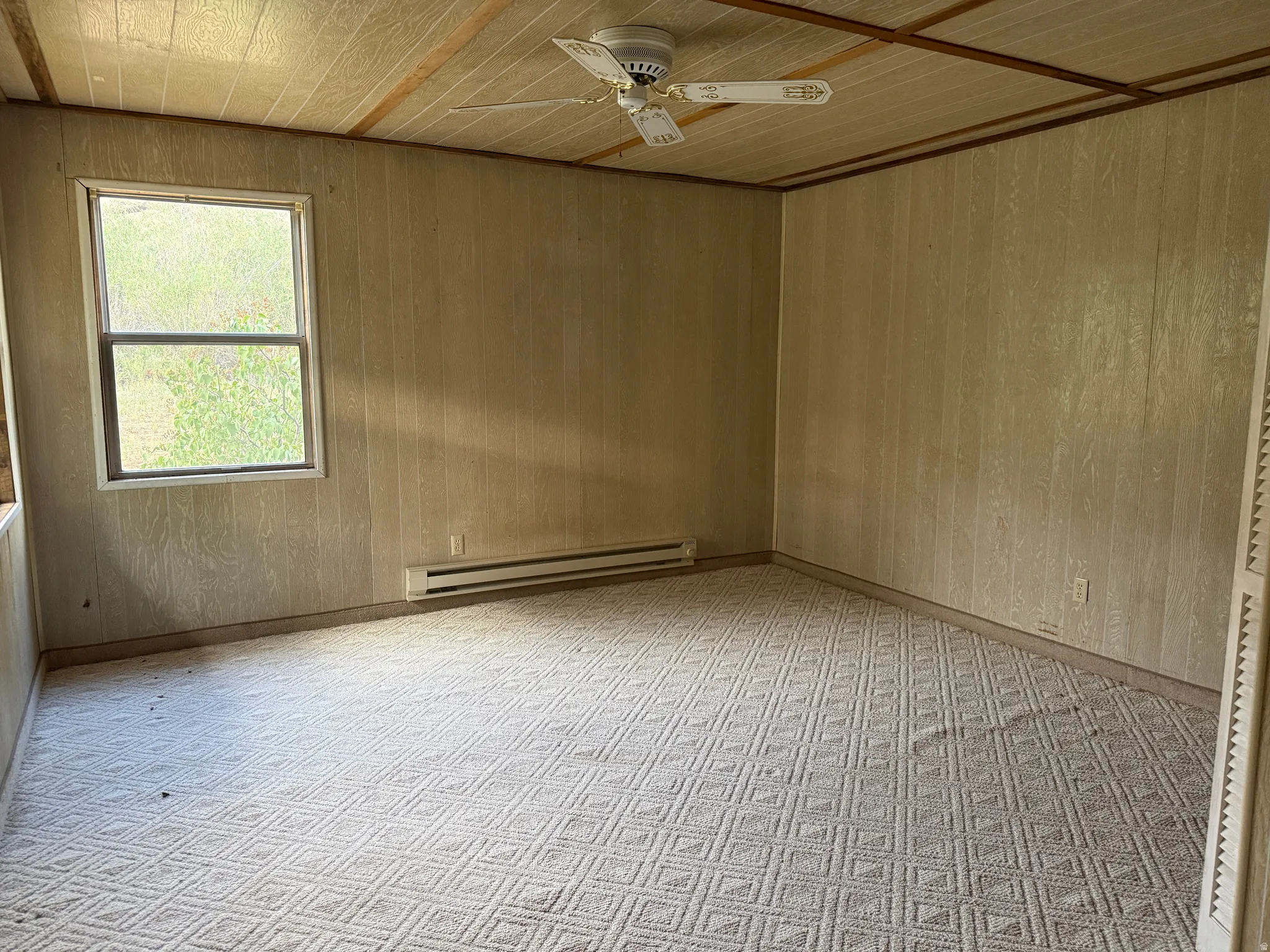 Carpeted room featuring a ceiling fan, wall paneling, and a window
