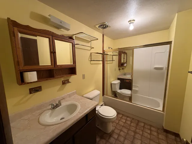 Bathroom featuring a vanity with an integrated sink, a medicine cabinet, an enclosed bathtub with shower, and patterned flooring