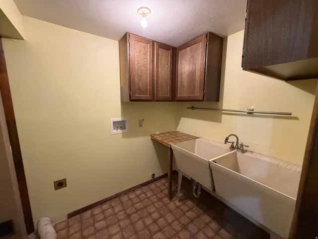 Utility room featuring a double basin sink, overhead cabinetry, and laundry hookups