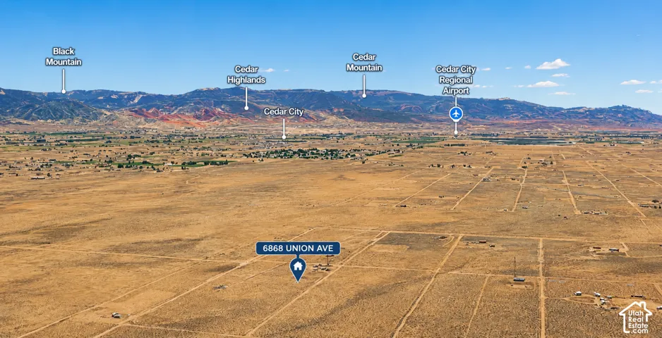 Expansive arid landscape featuring a prominent mountainside backdrop, with distant visible structures and a clear blue sky