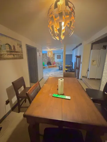 Dining area featuring a contemporary pendant light fixture, a wood-finish dining table, and direct sightlines to a separate living space with a stone-clad wall and a second matching pendant light fixture