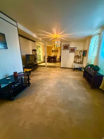 Spacious living area featuring large format tile flooring, a decorative ceiling light fixture, and white wall paneling