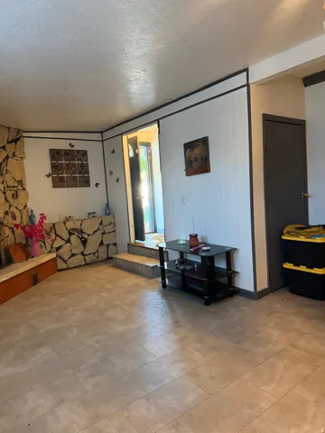 Living space featuring a stone-clad fireplace, built-in hearth, plank-style tile flooring, vertical paneling, and an entry door with sidelights