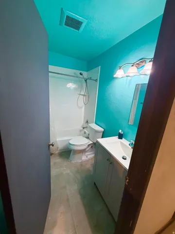 Bathroom with a single vanity featuring a white countertop and base cabinetry, a white toilet, and a white bathtub with shower