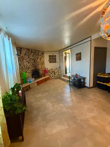 Spacious living area featuring a stone fireplace with a built-in hearth, rectangular light-toned tile flooring, and a window with sheer curtains