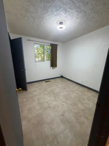 Bright room featuring a window with exterior tree views, light-toned tiled flooring, white walls, and a ceiling-mounted light fixture