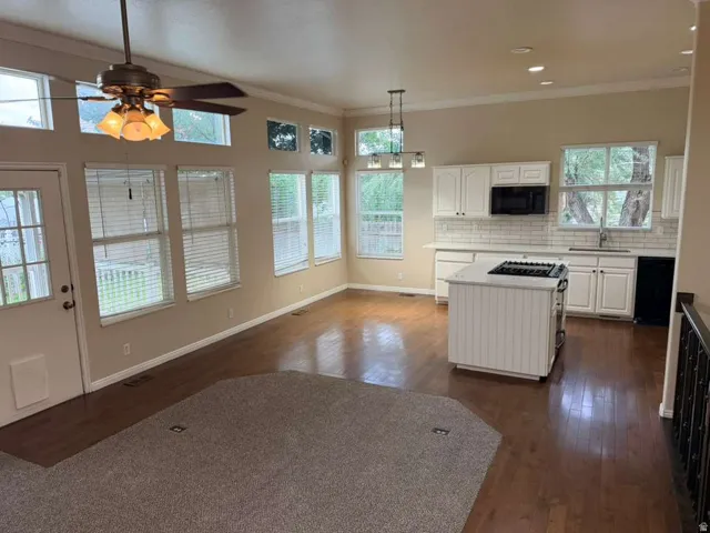 Open-concept living space featuring wood-finish flooring, a kitchen island with a cooktop, white cabinetry, a subway tile backsplash, and a ceiling fan with integrated lighting