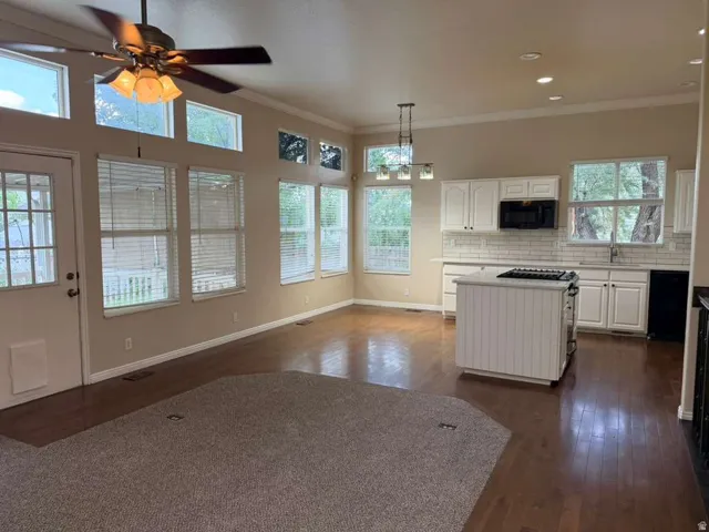 Open-concept living space featuring wood-finish flooring, a kitchen island with a gas cooktop, white cabinetry, subway tile backsplash, and extensive windowing with transom details
