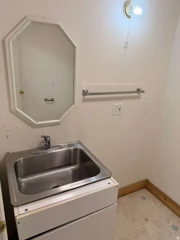 Utility room featuring a stainless steel sink, octagonal mirror, wall-mounted light fixture, and tile flooring