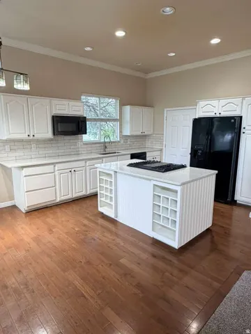 Kitchen featuring a central island with built-in shelving, white cabinetry, light countertops, wood-finish flooring, and recessed lighting