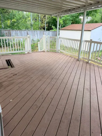 Spacious outdoor deck featuring composite wood-finish flooring, white railing, and a covered patio structure