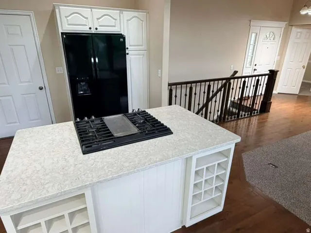 Kitchen island featuring an integrated gas stovetop, white cabinetry with black hardware, and an appliance pantry