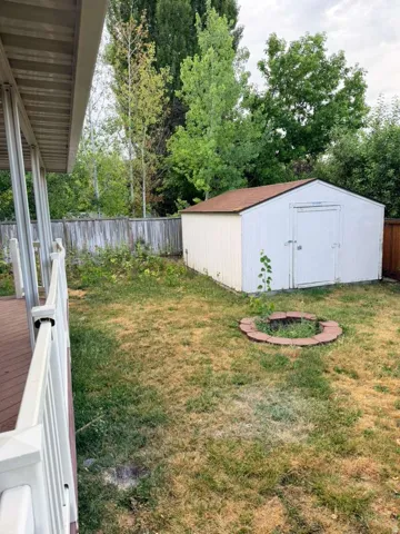Backyard area featuring a white storage shed with a brown roof, a brick-lined fire pit, and a wooden privacy fence