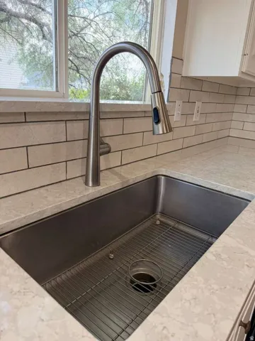 Stainless steel undermount sink with a gooseneck pull-down faucet, set into a light-toned countertop, complemented by a subway tile backsplash and a window