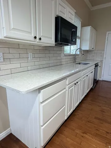Kitchen featuring white cabinetry, light-toned countertops, a subway tile backsplash, an undermount sink with a gooseneck faucet, and wood-finish flooring