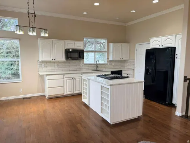 Kitchen featuring an island with built-in shelving, white cabinetry, subway tile backsplash, and wood-finish flooring
